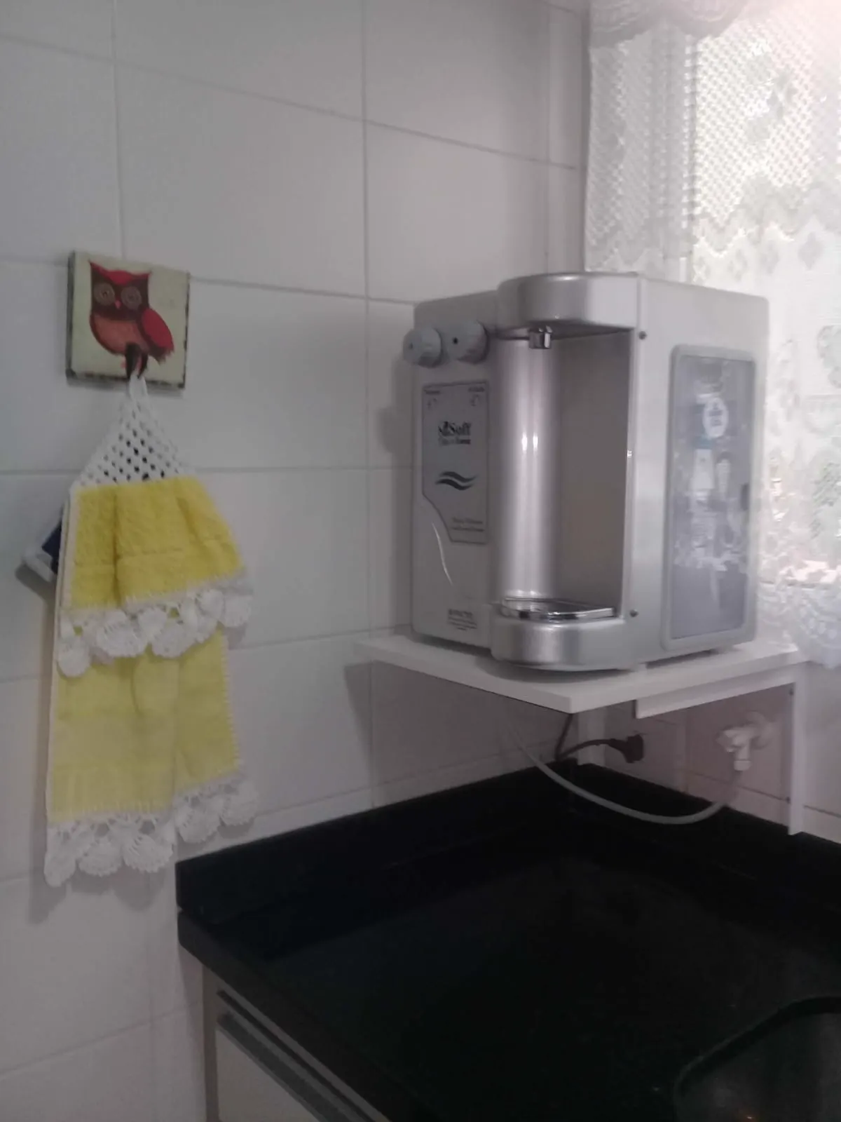 Purificador de água prata instalado sobre prateleira em cozinha residencial