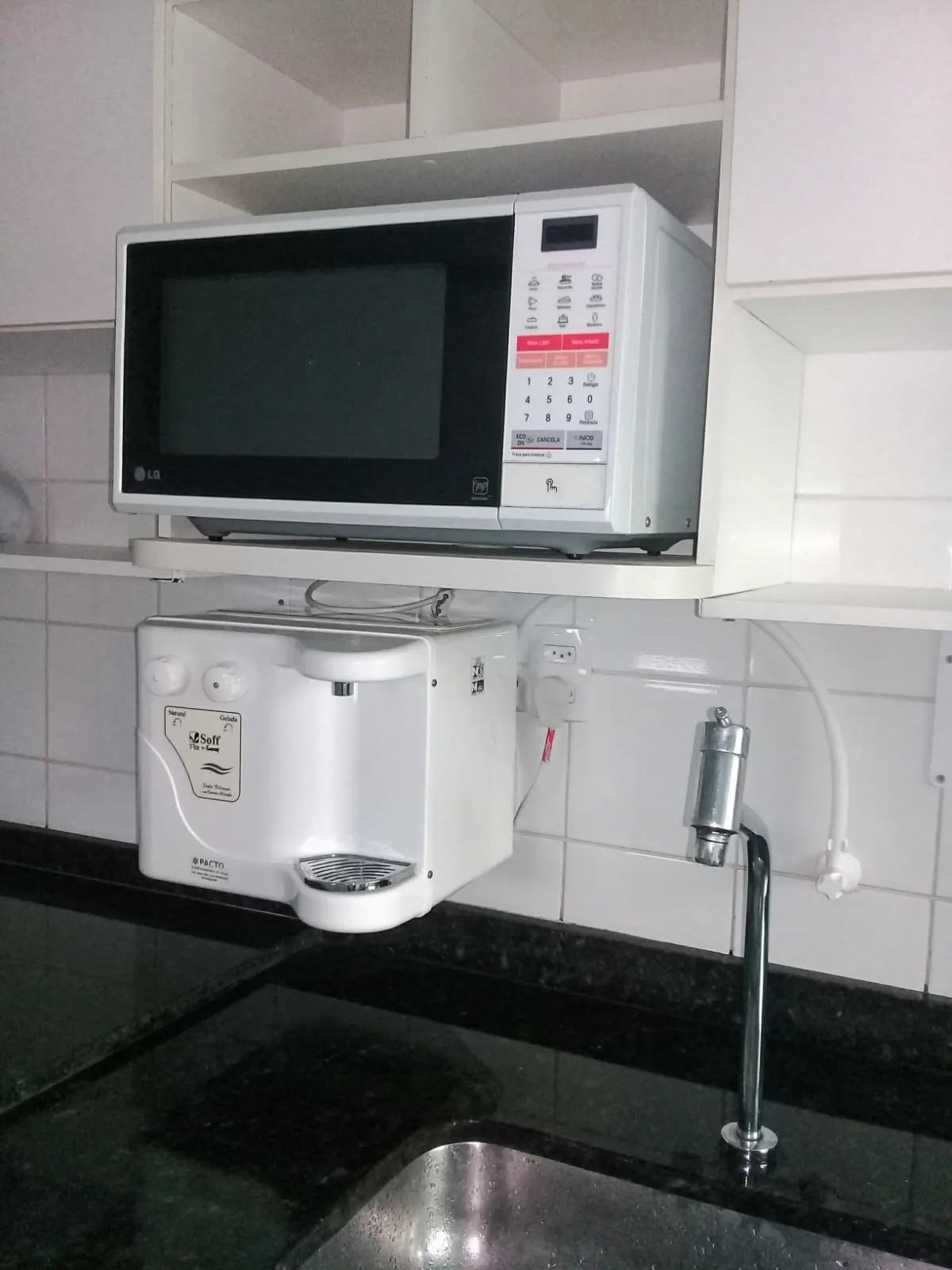 Purificador de água branco instalado na parede abaixo do micro-ondas, com torneira própria
