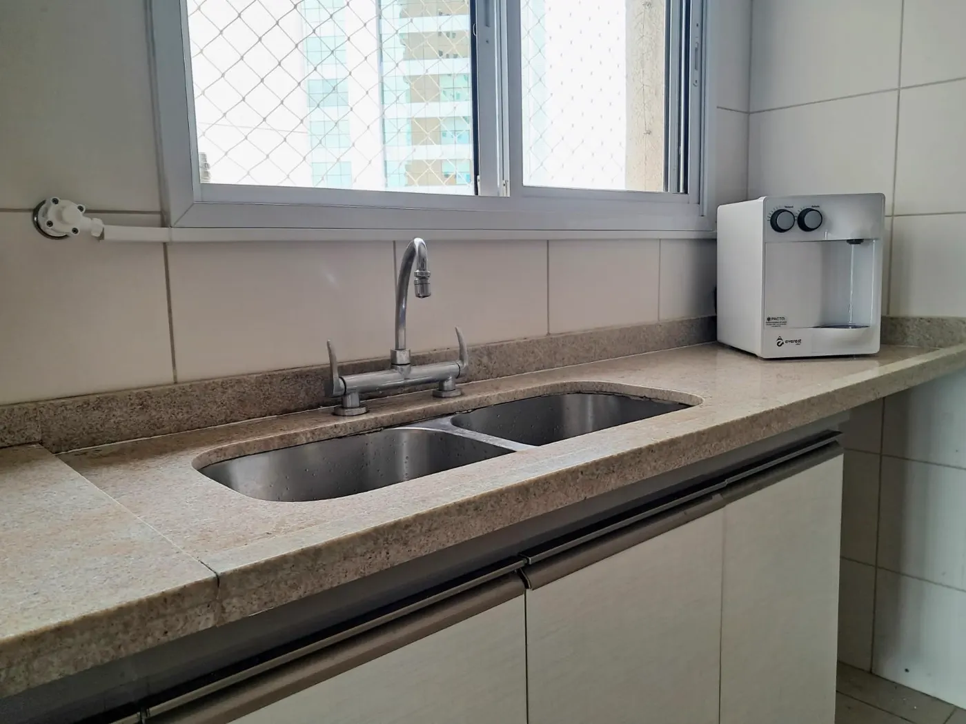 Purificador de água branco sobre bancada de granito ao lado da pia da cozinha