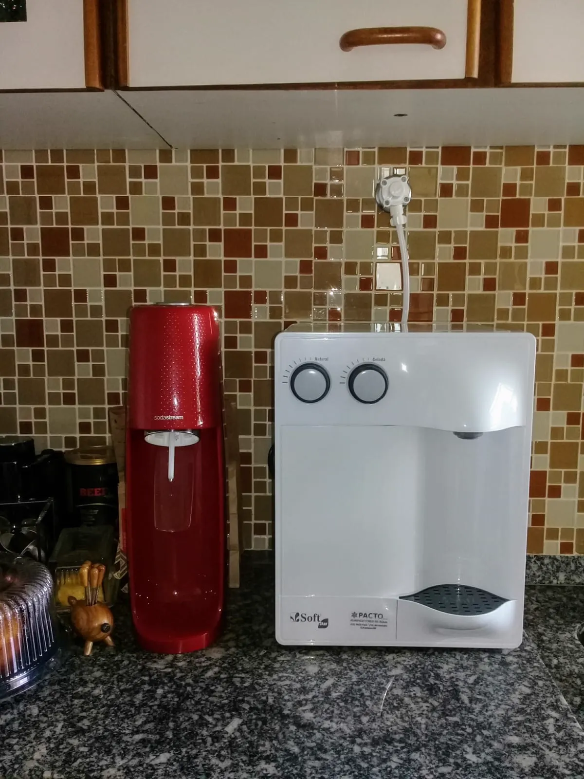 Purificador de água branco sobre bancada de granito em cozinha com pastilhas coloridas