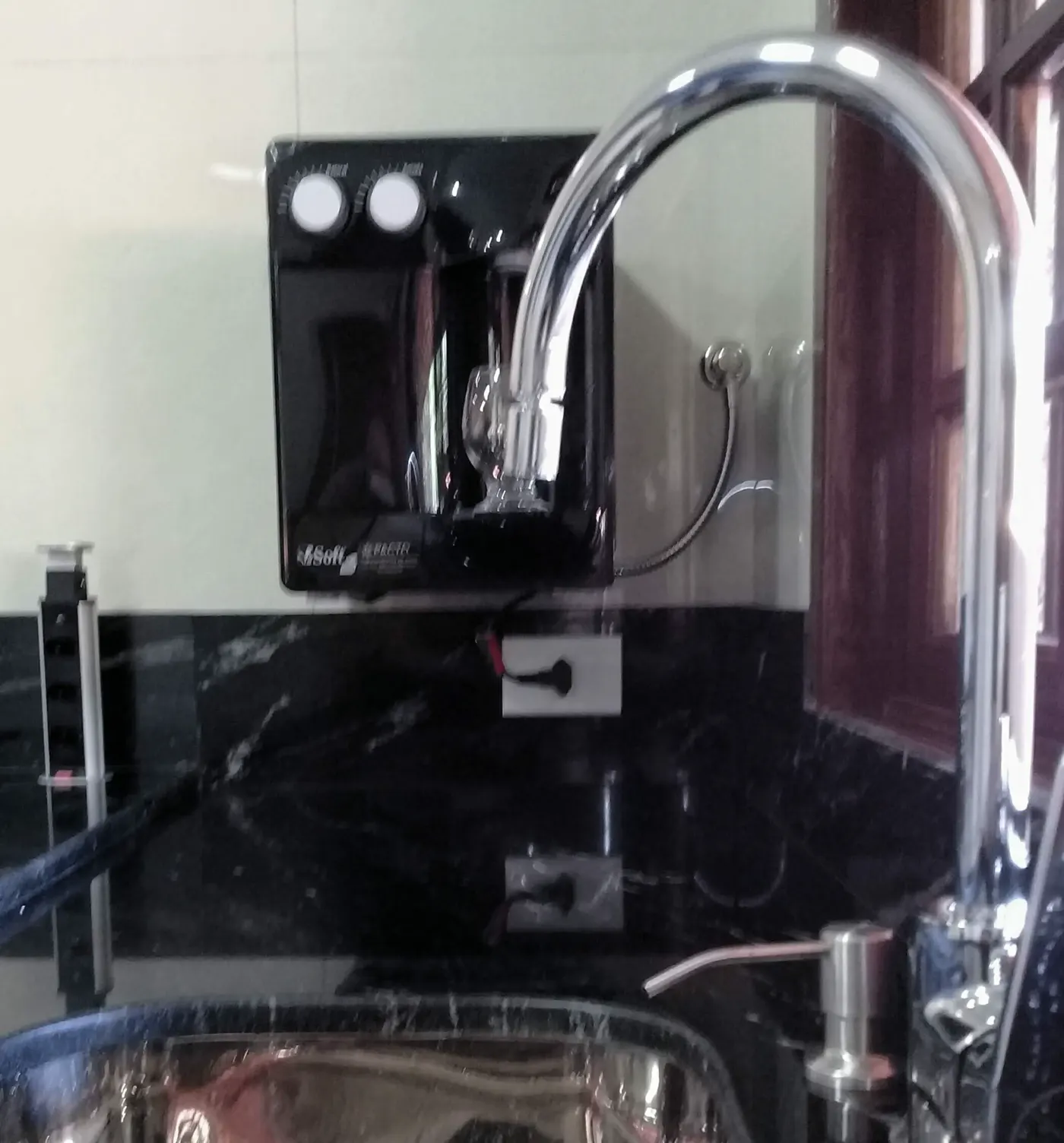 Purificador de água preto instalado na parede ao lado da torneira da pia