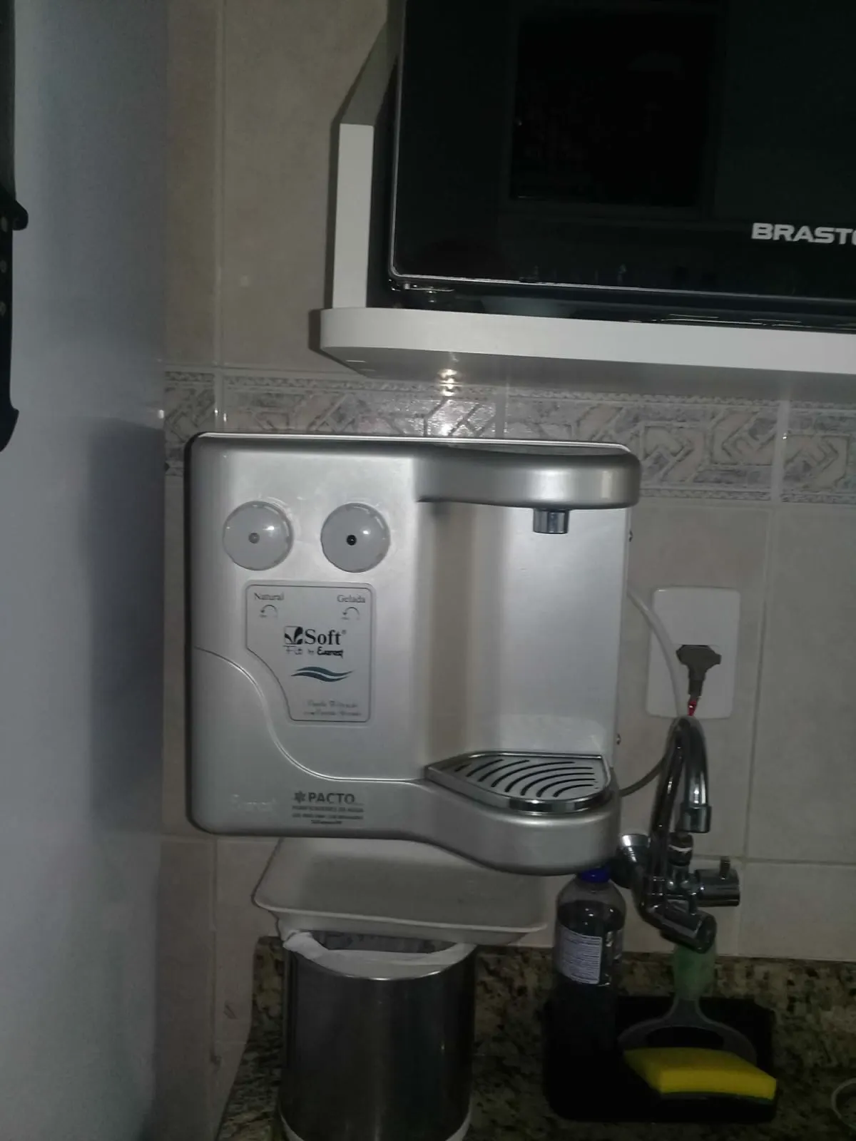 Purificador de água prata instalado em parede de cozinha próximo à torneira da pia